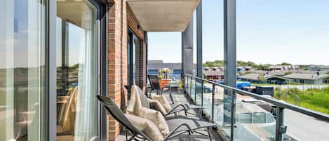 A balcony with outdoor seating, a glass railing, and a view of the surrounding neighborhood.
