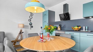 Una cocina moderna con una mesa redonda de madera, sillas tapizadas en gris y una lámpara colgante azul y amarilla.