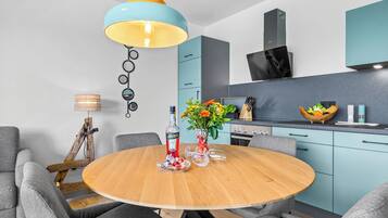 Een moderne keuken met een ronde houten tafel, grijze bekleden stoelen en een blauwgele hanglamp.