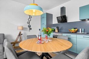 Eine moderne Küche mit einem runden Holztisch, grau gepolsterten Stühlen und einer blau-gelben Pendelleuchte.