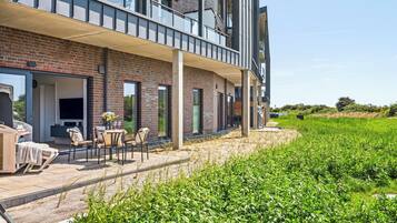Een modern gebouw met een bakstenen gevel, grote ramen en een balkon met zitplaatsen.