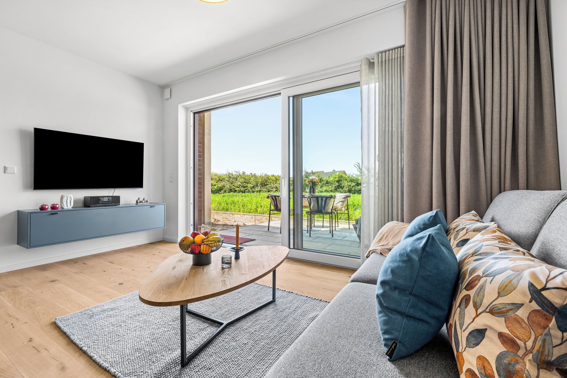 Een moderne woonkamer met een flatscreen televisie, een blauwe console, een houten salontafel en een bank met gekleurde kussens.