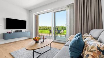 Een moderne woonkamer met een flatscreen televisie, een blauwe console, een houten salontafel en een bank met gekleurde kussens.