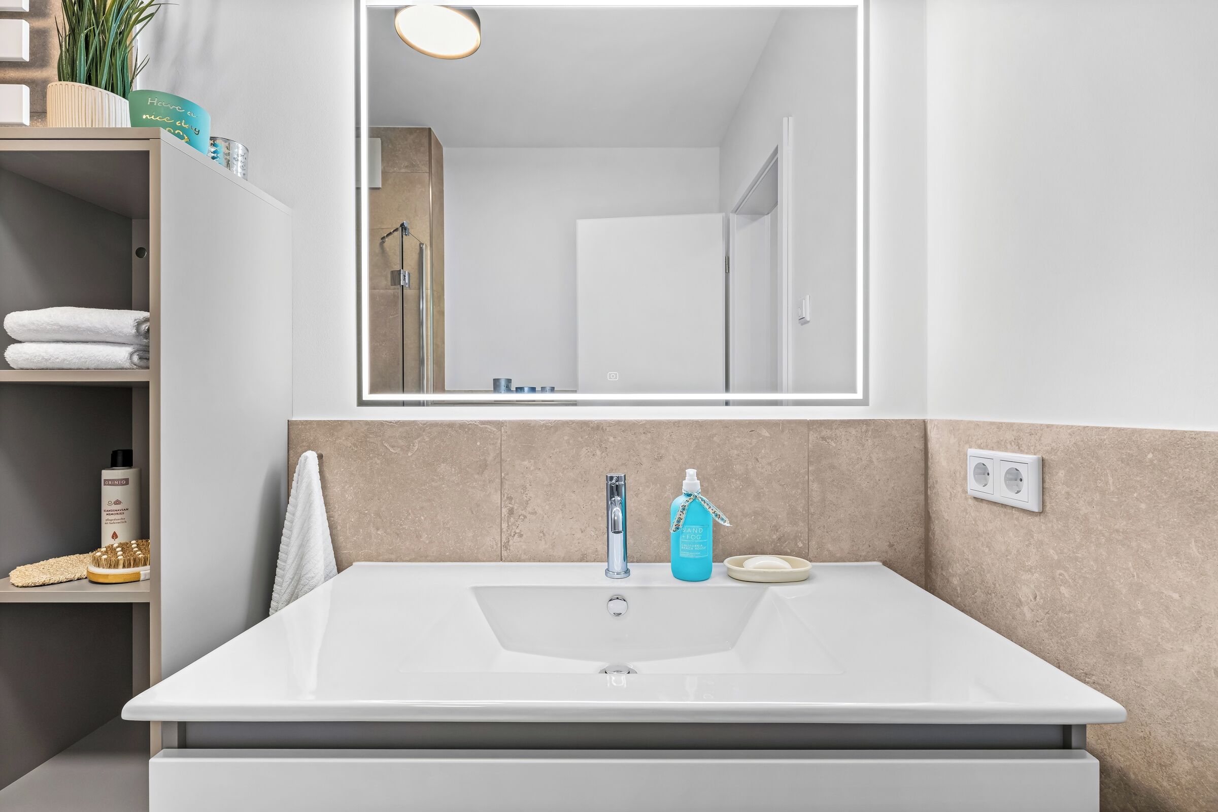 A bathroom with a white sink, a mirror, and a shelf with toiletries.
