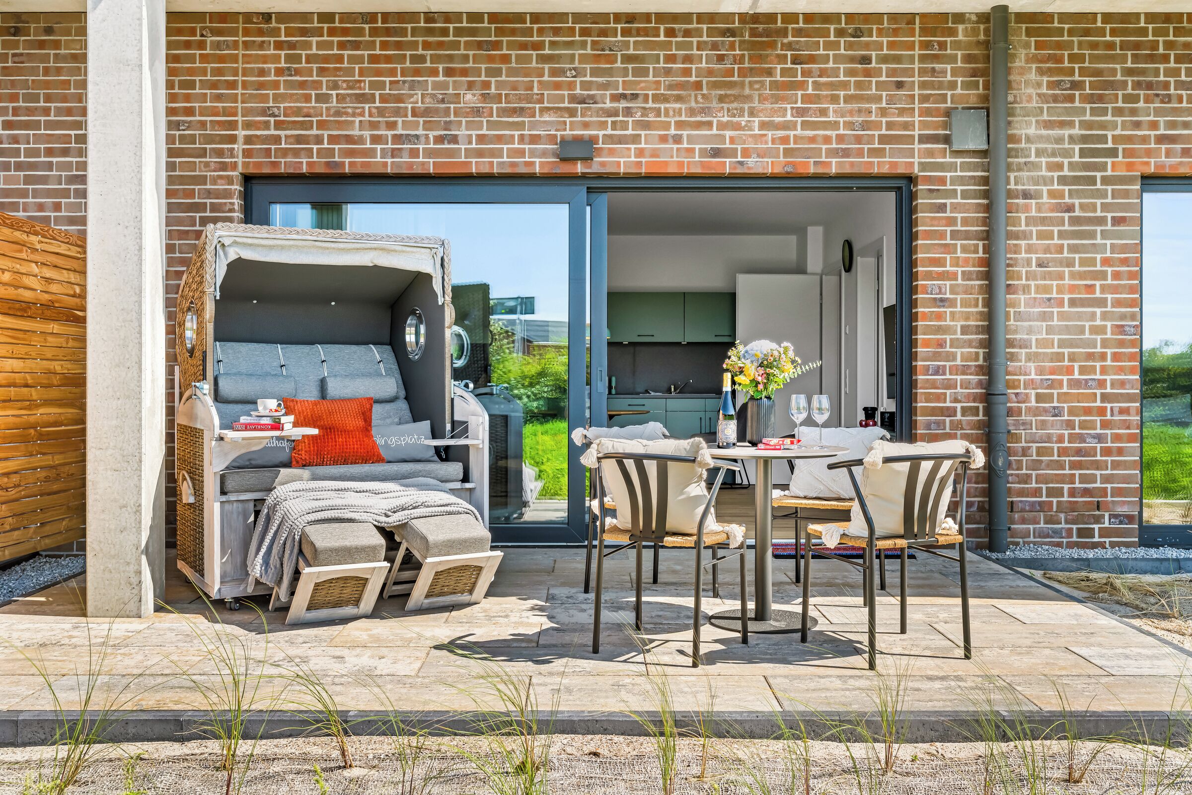 Un espacio exterior moderno con una zona de estar cubierta, una mesa de comedor y vistas al interior de la casa.