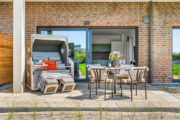 A modern outdoor living space with a covered seating area, a dining table, and a view into the house. - The View B01 Watt'n Glück -Terrace,garden furniture, shared Sauna, parking space (Dagebüll)