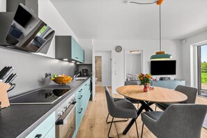 Eine moderne Küche mit einer zentralen Kochinsel, einem Essbereich mit rundem Tisch und einem an der Wand befestigten Fernseher.
