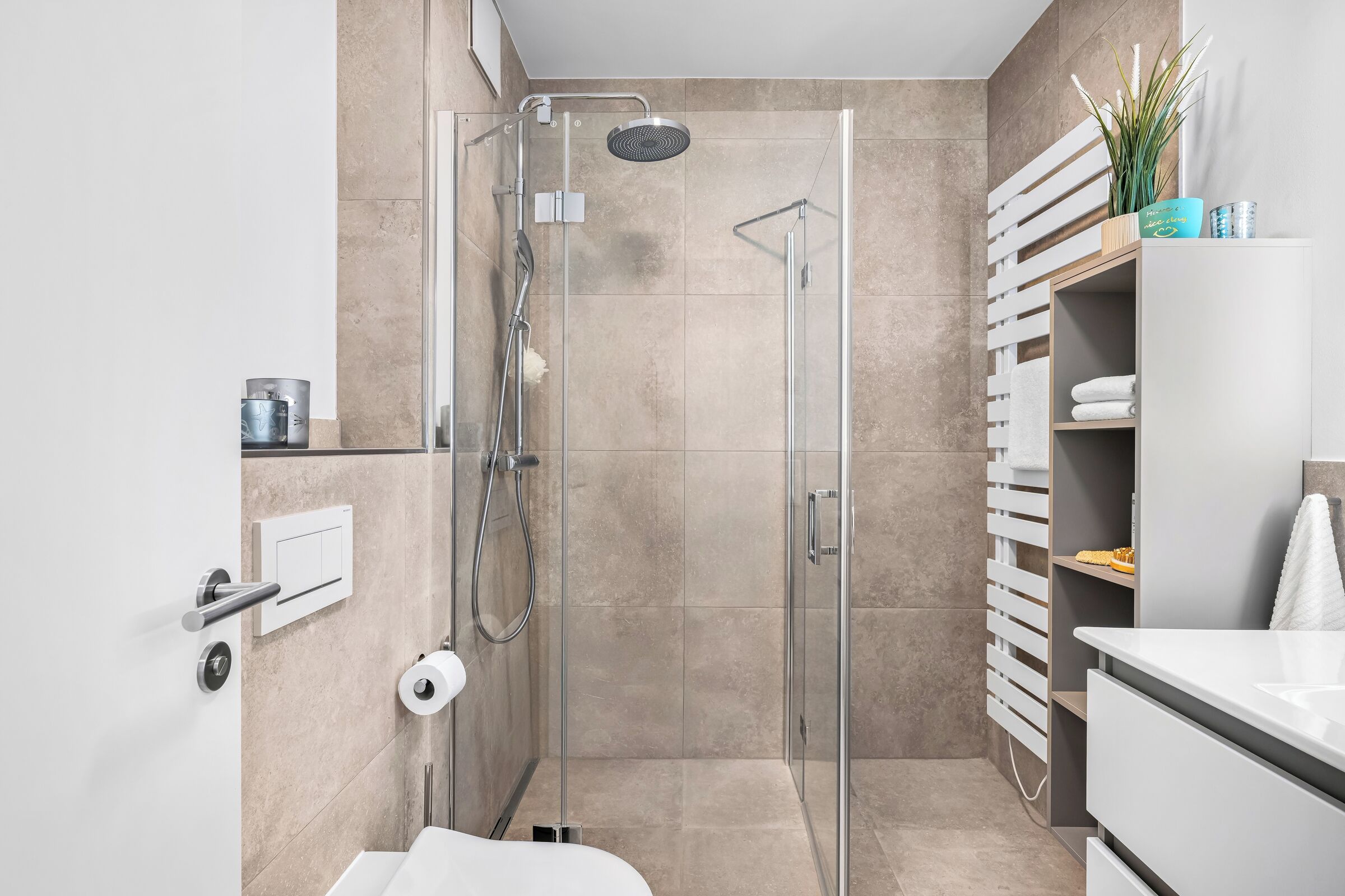 Ein modernes Badezimmer mit einer Glaskabine zur Dusche, einem weißen Waschbecken und einem Handtuchhalter.