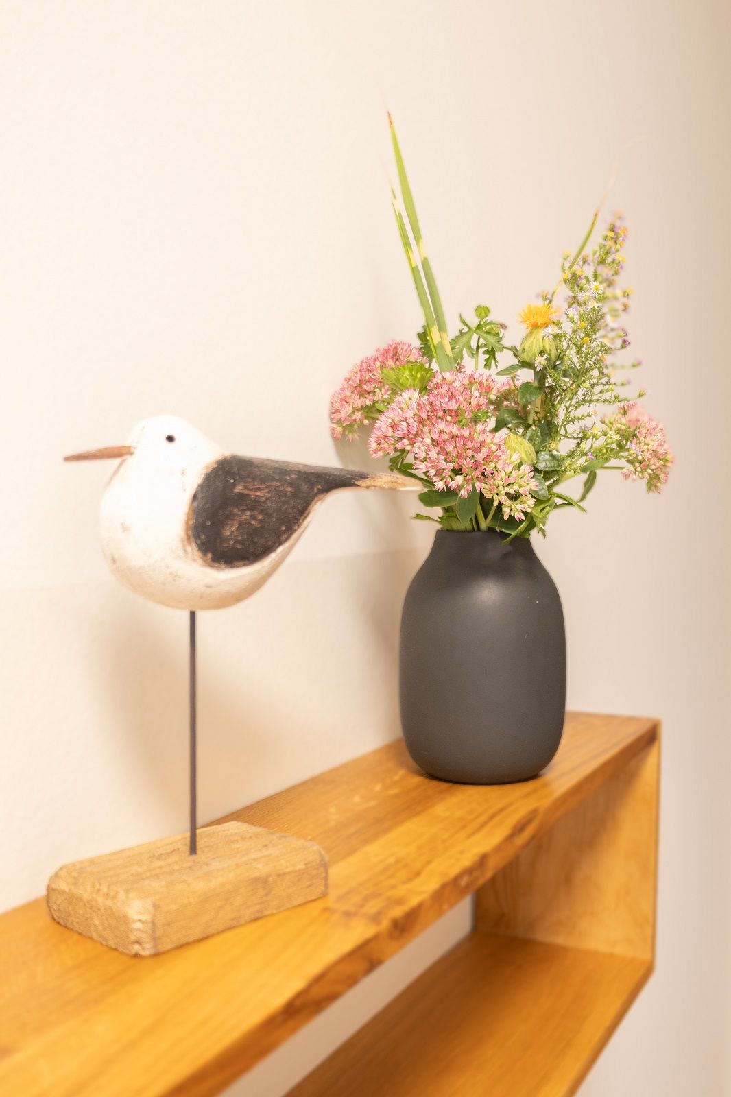 Een vogelvormige sculptuur met een bloevas op een houten plank.