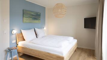 Une chambre avec un lit en bois, un mur bleu, un tableau, un luminaire en fibres tressées et un téléviseur fixé au mur.