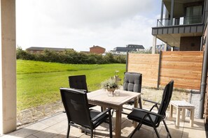 Un patio exterior con una mesa y sillas, una planta en maceta y vistas a un área con césped y edificios al fondo.
