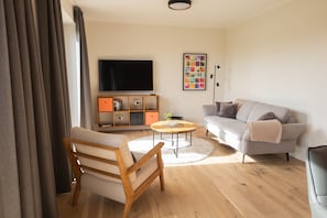 Ein modernes Wohnzimmer mit einer Couch, einem Holzstuhl, einem Couchtisch, einem Fernseher und einem Bücherregal.