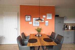 A dining area with a wooden table, six chairs, a vase with flowers, and wall art. - The View CO4 Meerzeit - Terrace, garden furniture, shared. Sauna, parking space (Dagebüll)