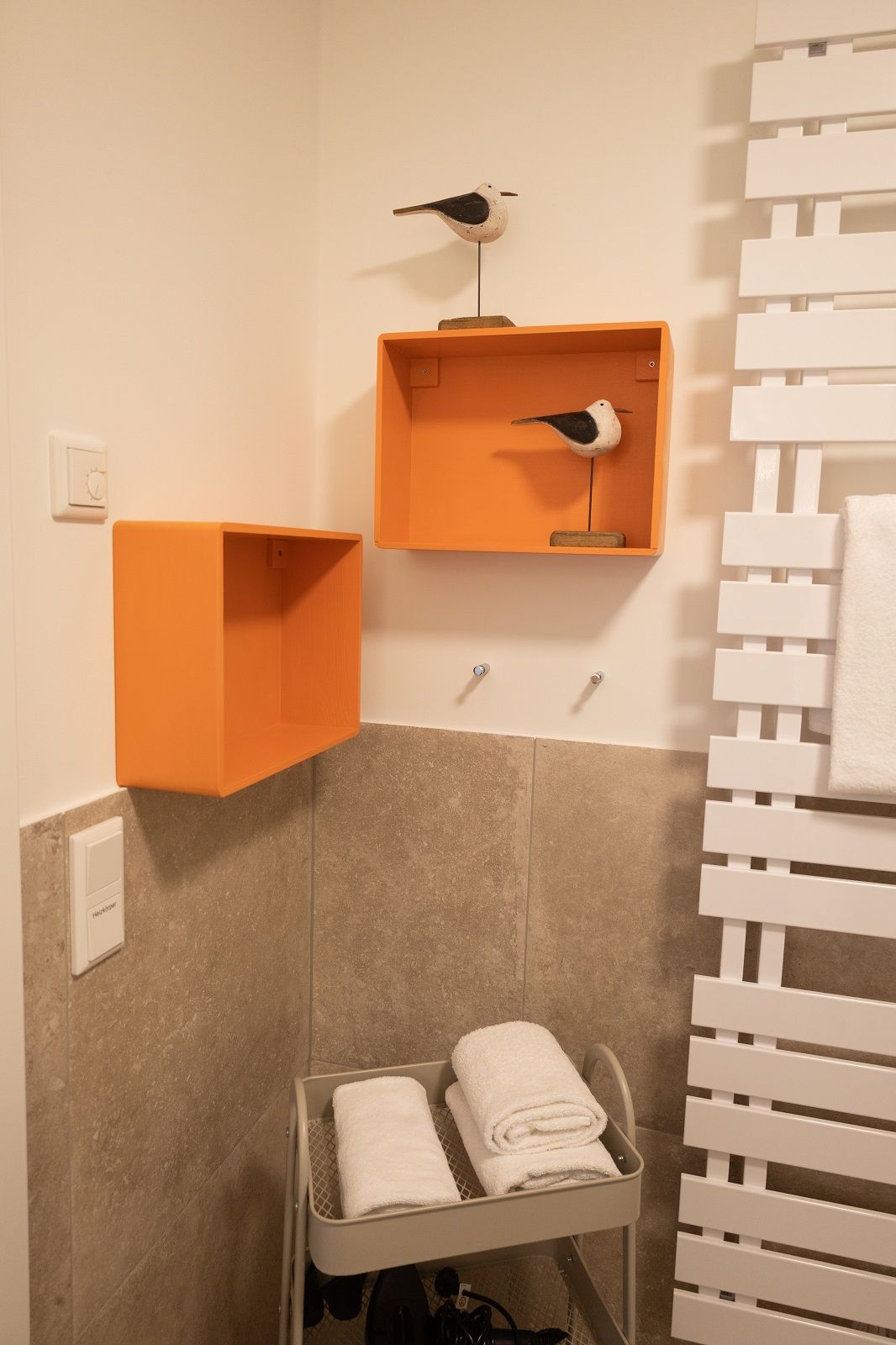 Une salle de bain équipée d’un porte-serviettes, d’un sèche-serviettes et d’une étagère décorée d’un motif d’oiseau.