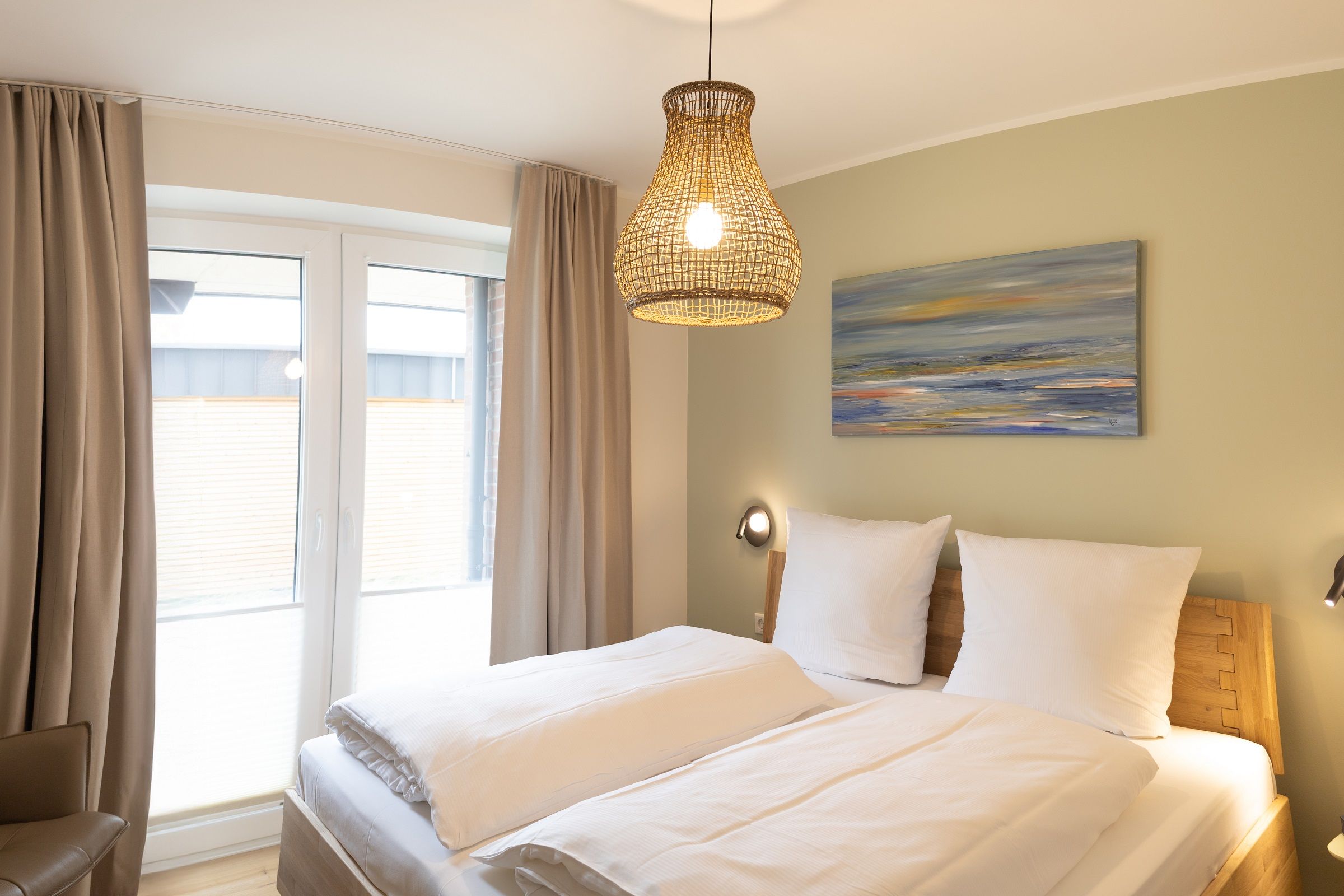 Una habitación de hotel con cama, cortinas, un cuadro y una lámpara colgante.