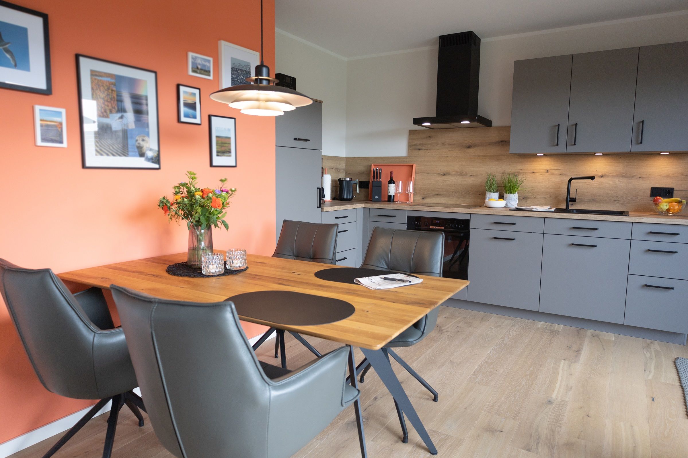 Une cuisine moderne avec des meubles gris, une table à manger en bois et un vase rempli de fleurs.