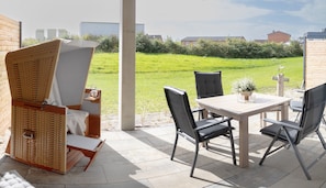 Un patio con una mesa y sillas, una silla de mimbre y vistas a un campo verde.