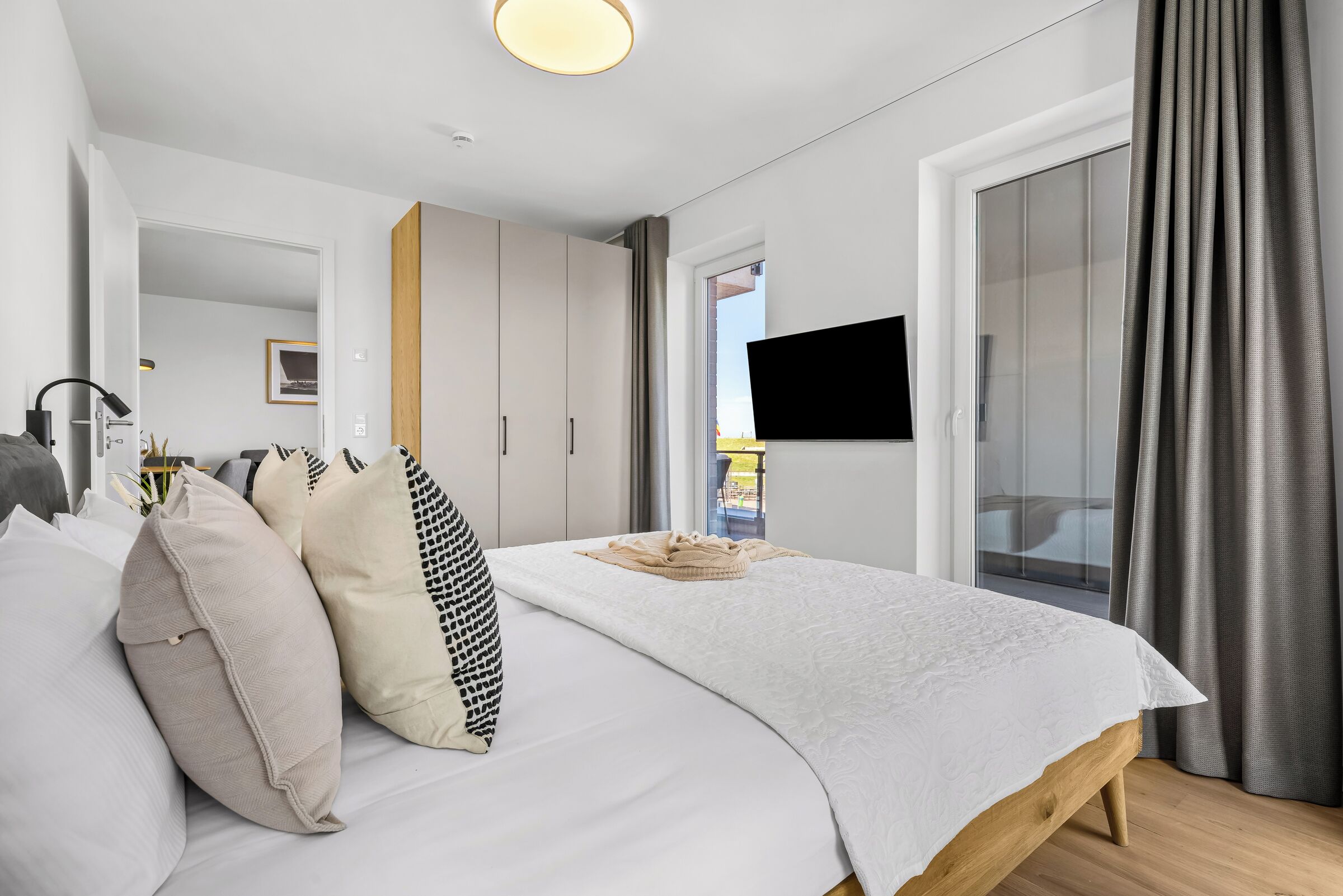 Ein modernes Schlafzimmer mit einem Bett, Kissen, einem Flachbildfernseher und einer Glastür, die zu einem Außenbereich führt.
