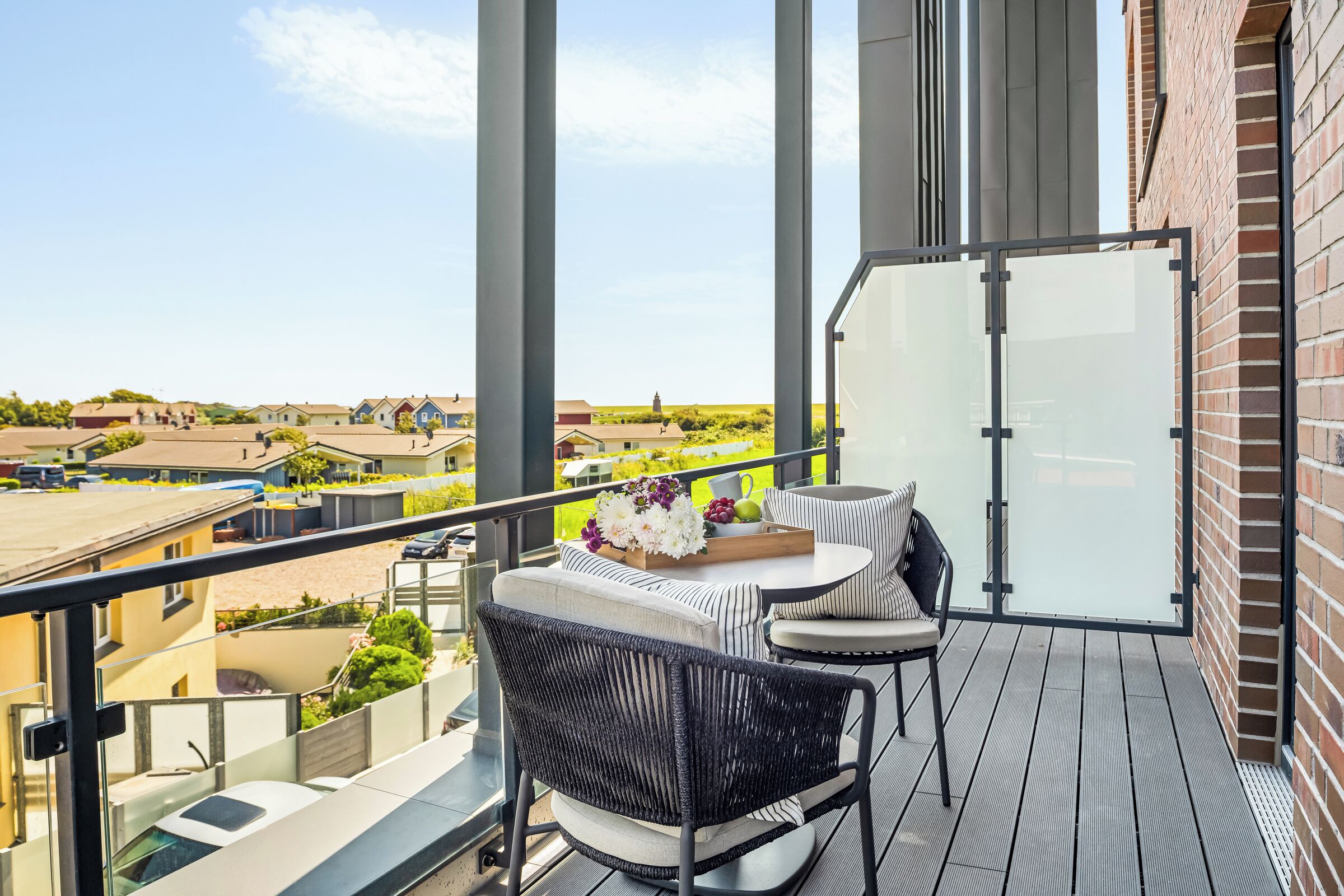 A balcony with a table and chairs, a glass door, and a view of a residential area.