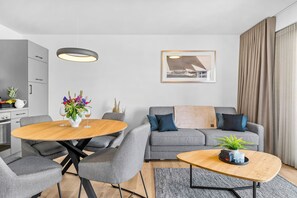 Ein modernes Wohnzimmer mit einem grauen Sofa, einem Holztisch und einem Essbereich mit einem runden Tisch und Stühlen.