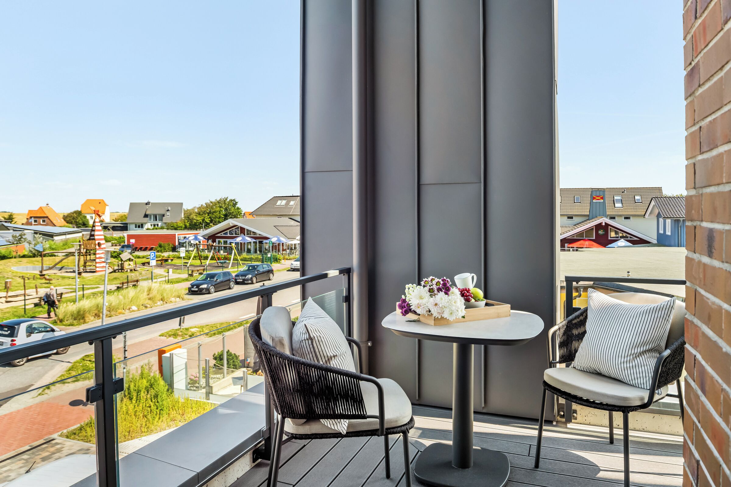 Een balkon met twee stoelen en een kleine tafel, met uitzicht op een straat met auto's en gebouwen.