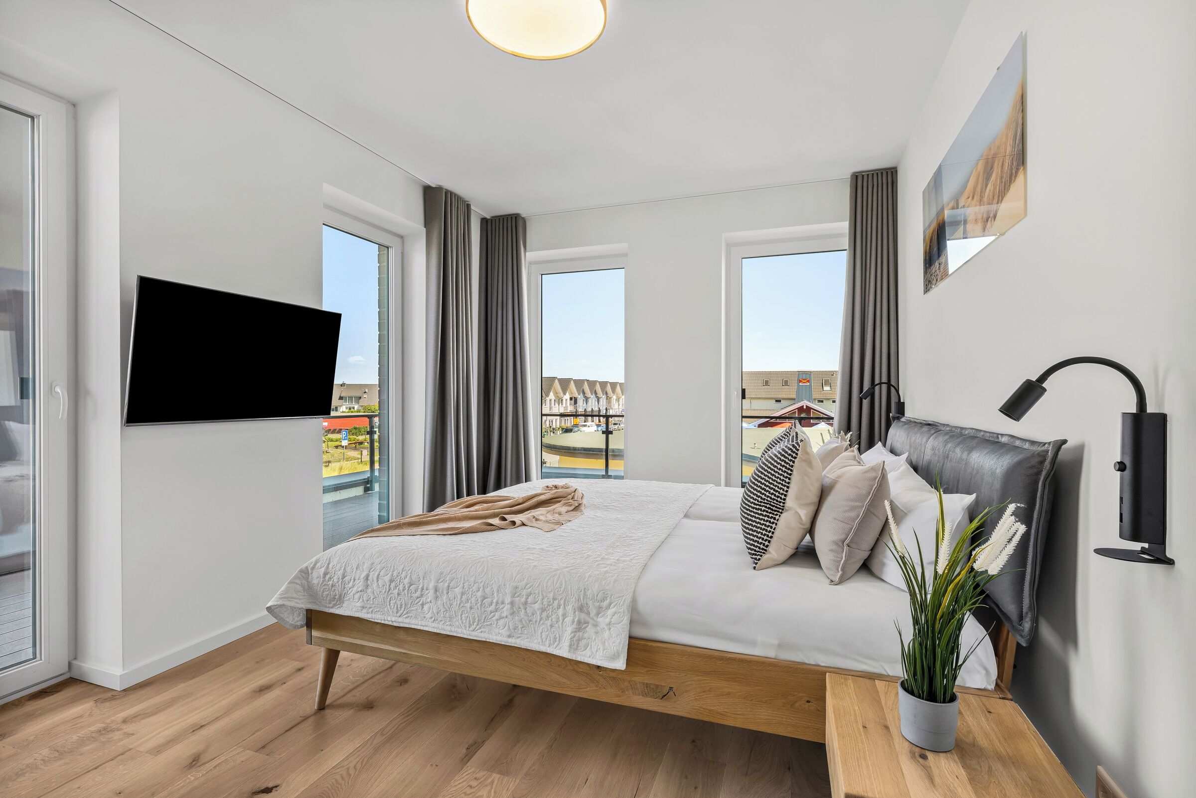 Ein modernes Schlafzimmer mit einem großen Bett, einem Wand-Fernseher und Blick auf die Stadt durch die Fenster.