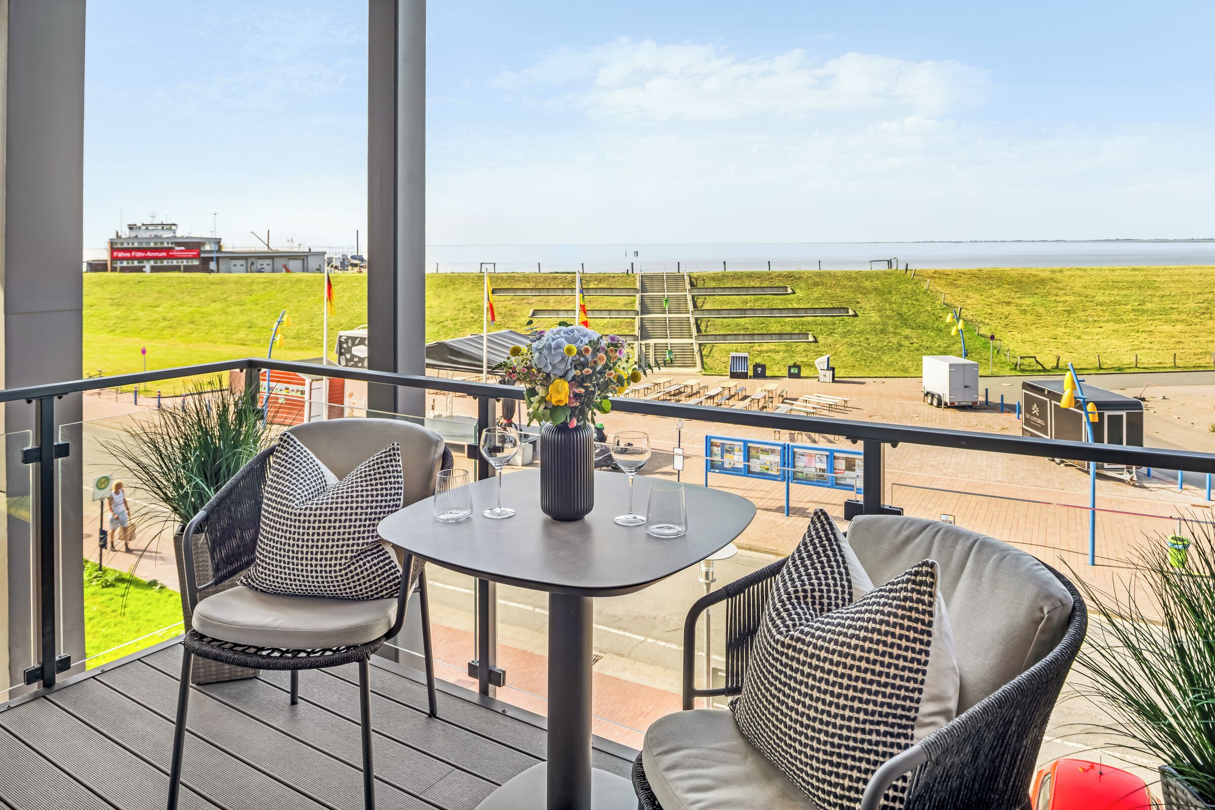 A balcony with a table and chairs, overlooking a grassy area and a body of water.