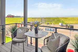 Un balcon avec une table et des chaises, donnant sur une zone herbeuse et un plan d’eau.