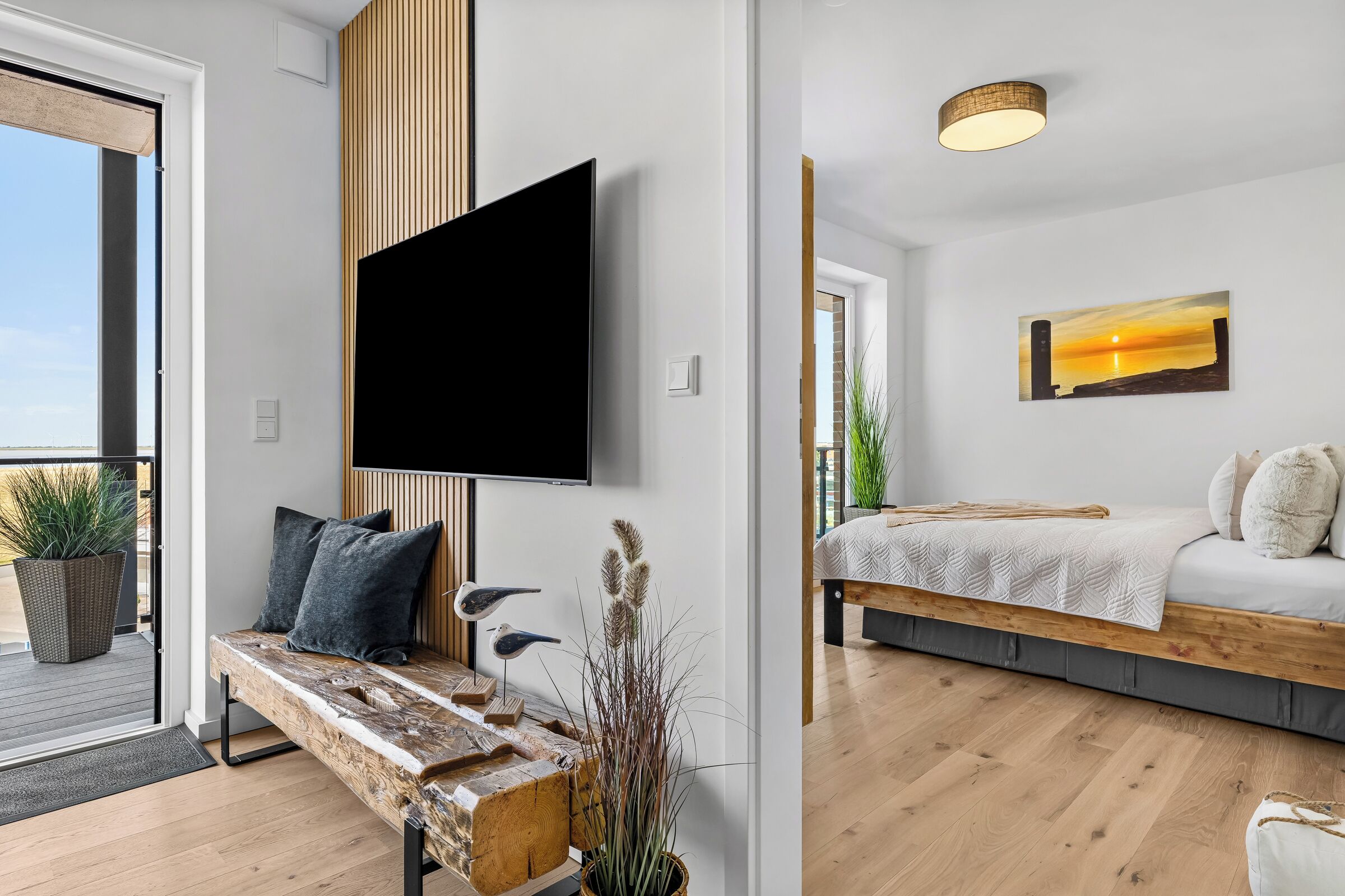 A modern living room with a flat-screen TV mounted on the wall, a wooden bench with cushions, and a bed with a white bedspread.