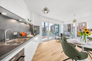 A modern kitchen with a built-in oven, a sink, and a dining area with a table and chairs. - The View A9 Auster – Sea view, shared sauna, elevator, parking space (Dagebüll)