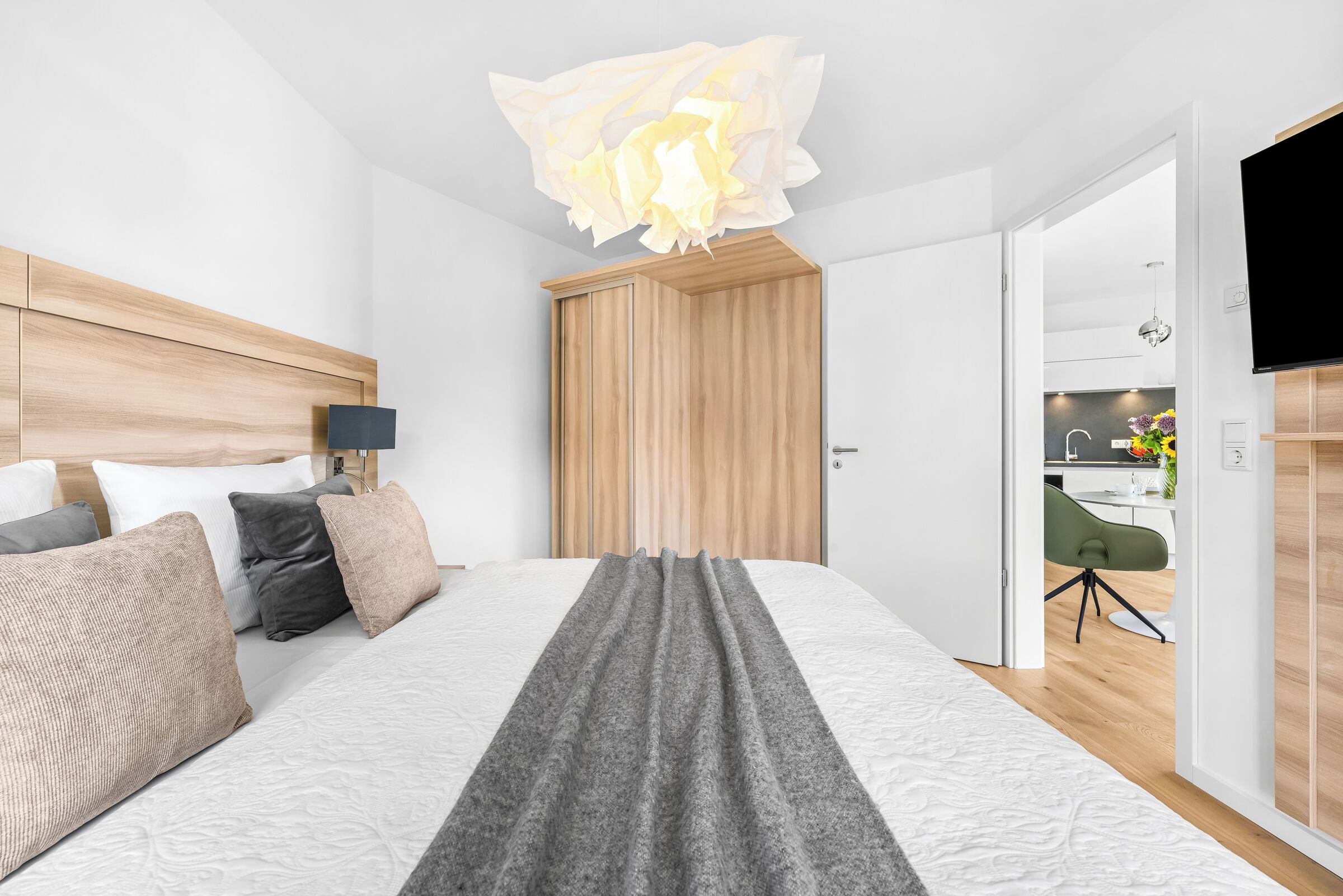 Een moderne hotelkamer met een groot bed, een houten hoofdeinde, een nachtkastje met een lamp en uitzicht op de keuken.