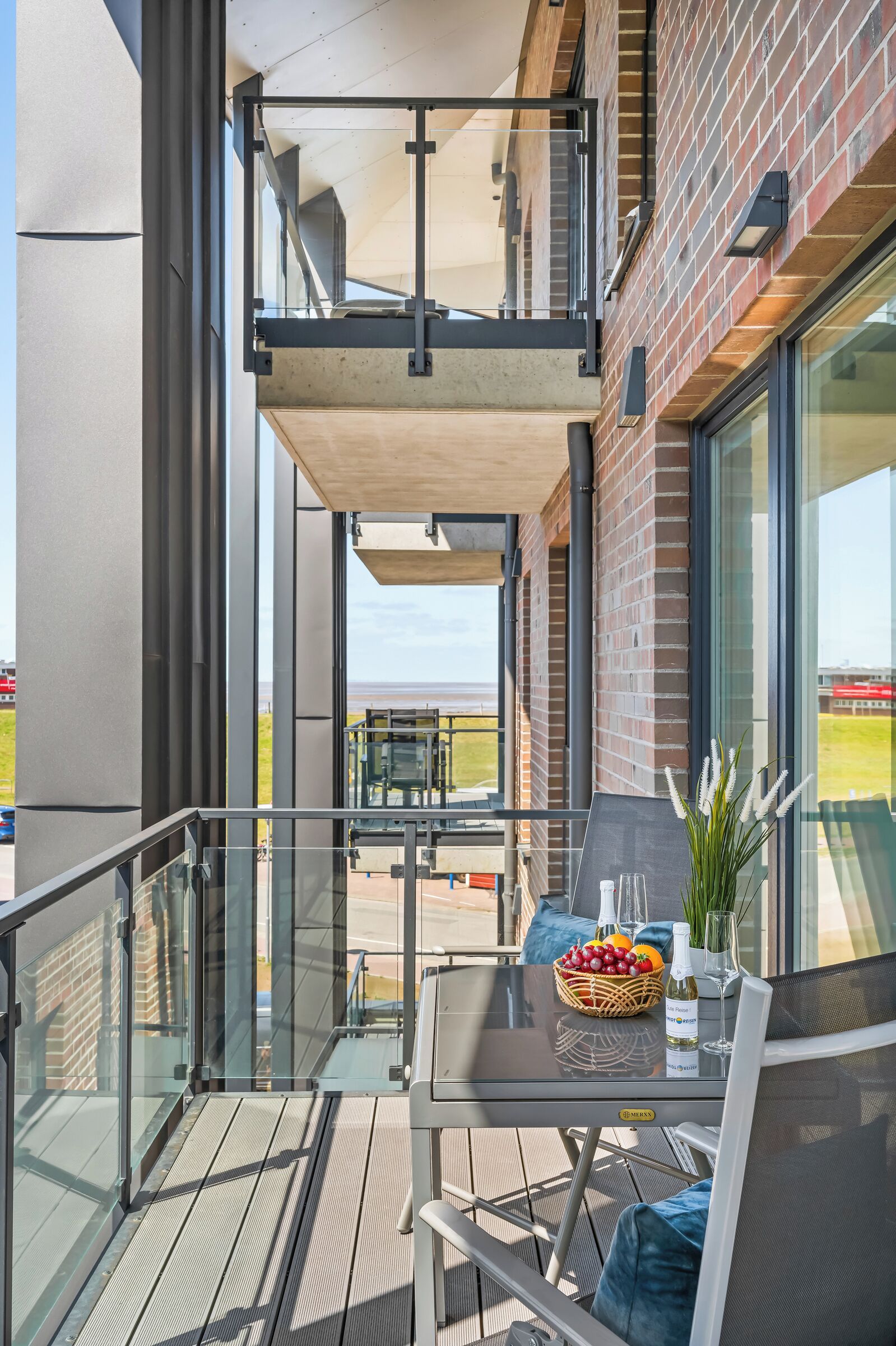 Een balkon met een tafel gedekt voor twee personen, een glazen hekwerk en uitzicht op een sportveld.