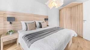 Une chambre à coucher moderne avec une tête de lit en bois, un grand lit avec une literie à motifs, des tables de chevet avec des lampes et une armoire en bois.
