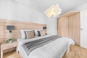 A modern bedroom with a wooden headboard, a large bed with patterned bedding, bedside tables with lamps, and a wooden wardrobe. - The View A9 Auster – Sea view, shared sauna, elevator, parking space (Dagebüll)