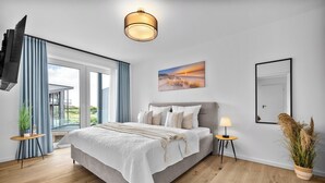 Ein Schlafzimmer mit Bett, Nachttisch, Lampe, einem Fenster mit Vorhängen, einem Bild und einer Topfpflanze.