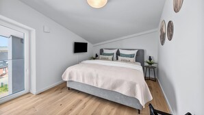 Ein modernes Schlafzimmer mit einem Bett, einem Flachbildfernseher und einem kleinen Nachttisch mit einer Pflanze.
