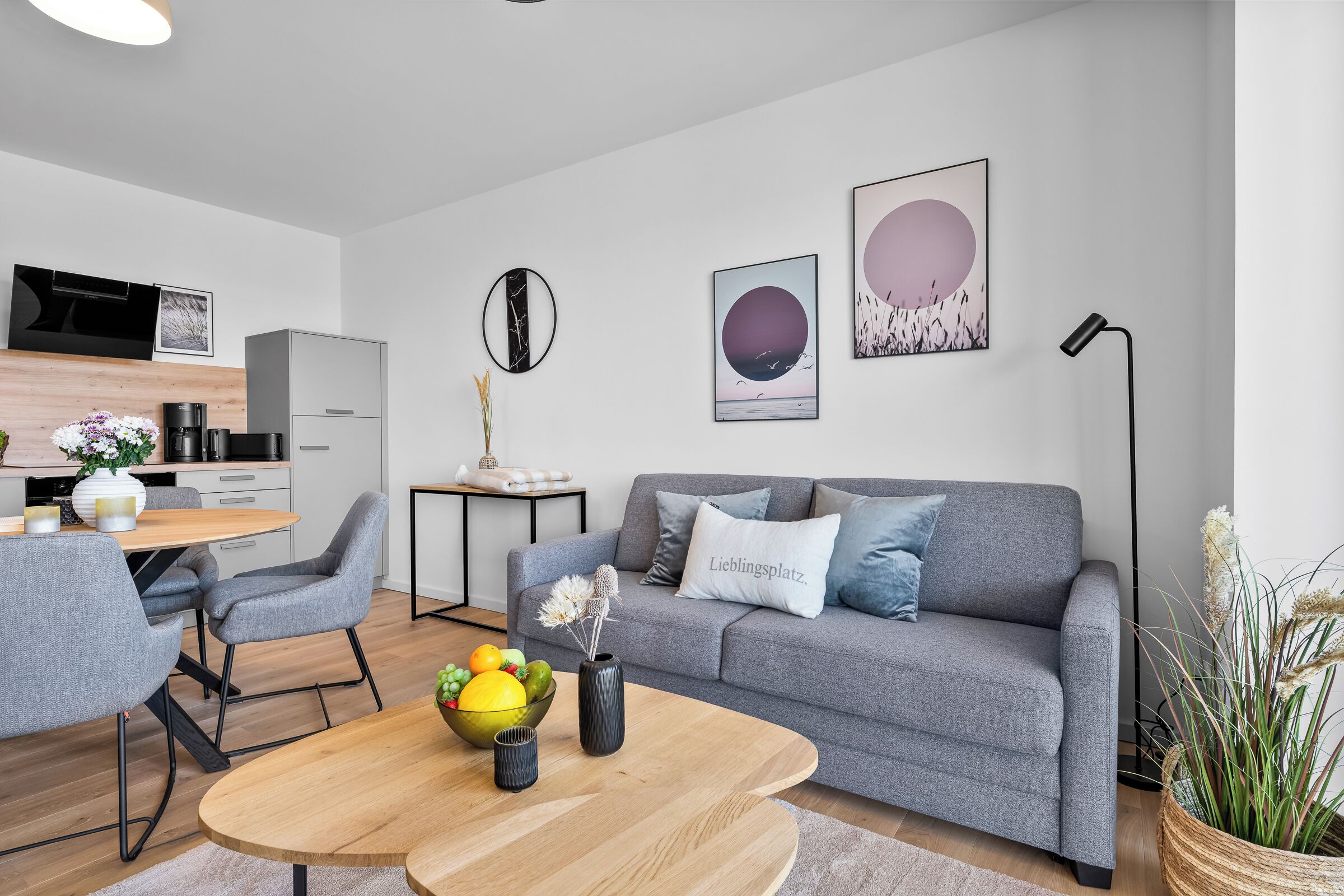 Una sala de estar moderna con un sofá gris, una mesa de centro redonda y un comedor con una mesa y sillas de madera.