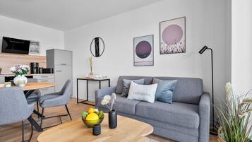 Una sala de estar moderna con un sofá gris, una mesa de centro redonda y un comedor con una mesa y sillas de madera.