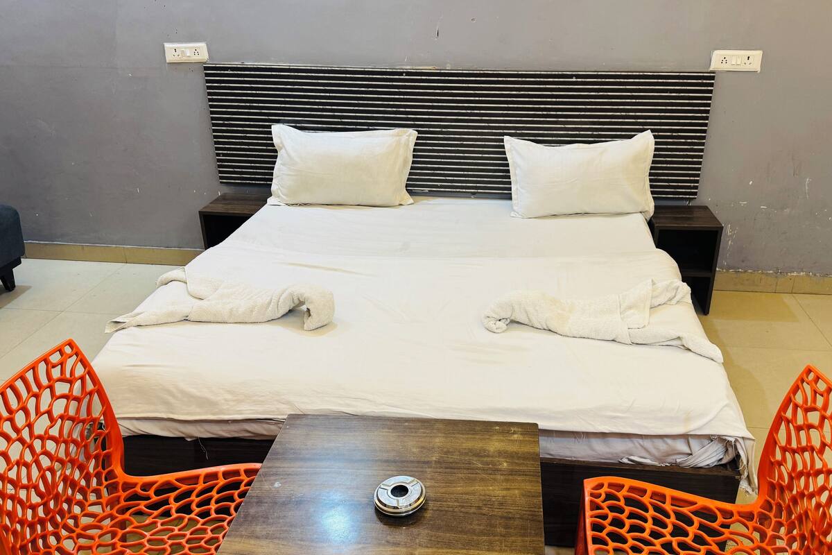 A neatly made bed with pillows, a bedside table with a cup, and two orange chairs.