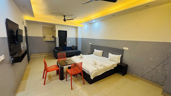A hotel room with a bed, a TV, a ceiling fan, and a seating area with chairs and a table.