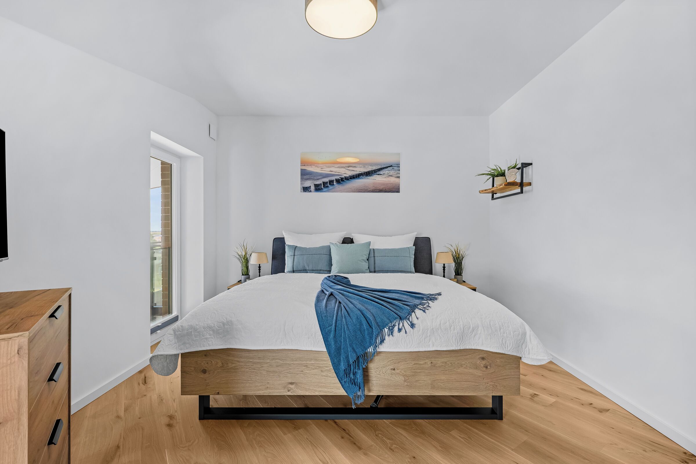 Ein modernes Schlafzimmer mit einem Bett, einem Gemälde, einem Regal mit Pflanzen und einem Fenster.