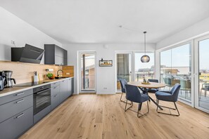 Eine moderne Küche mit grauen Schränken, einer Holz Arbeitsplatte und einem Essbereich mit rundem Tisch und blauen Stühlen.
