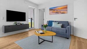 Una sala de estar moderna con un televisor de pantalla plana, un sofá gris y un cuadro de una puesta de sol.