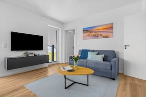 Ein modernes Wohnzimmer mit Flachbildfernseher, grauem Sofa und einem Sonnenuntergangsbild.
