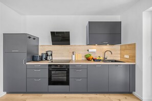 Eine moderne Küche mit grauen Schränken, einem Einbauofen, einer Kaffeemaschine und einem Spülbecken mit Holz Arbeitsplatte.