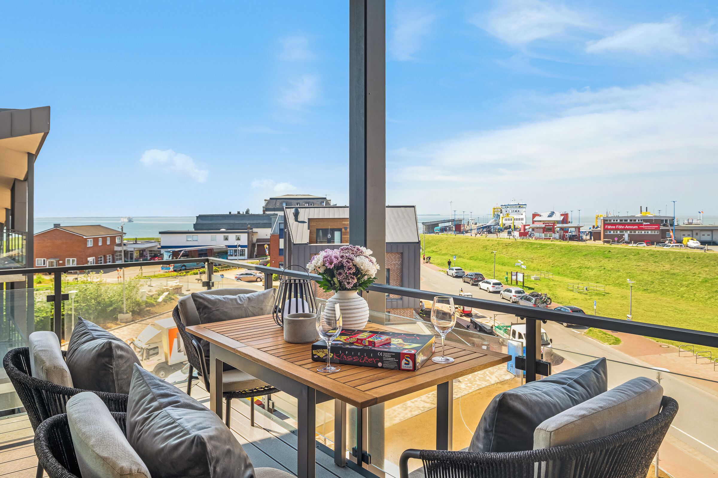 Ein Balkon mit Tisch, Stühlen und Blick auf das Meer und einen Hafen.
