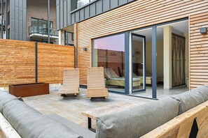 A modern outdoor seating area with a wooden deck, a built-in bench, and a glass door leading to a room. - The View A15 Mole 15 - Sea view, common. Sauna, elevator, dog-friendly, parking (Dagebüll)