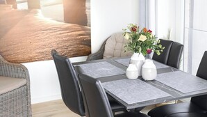 Un comedor moderno con una mesa dispuesta para cuatro personas, rodeada de sillas negras, una silla de mimbre y un florero con flores.