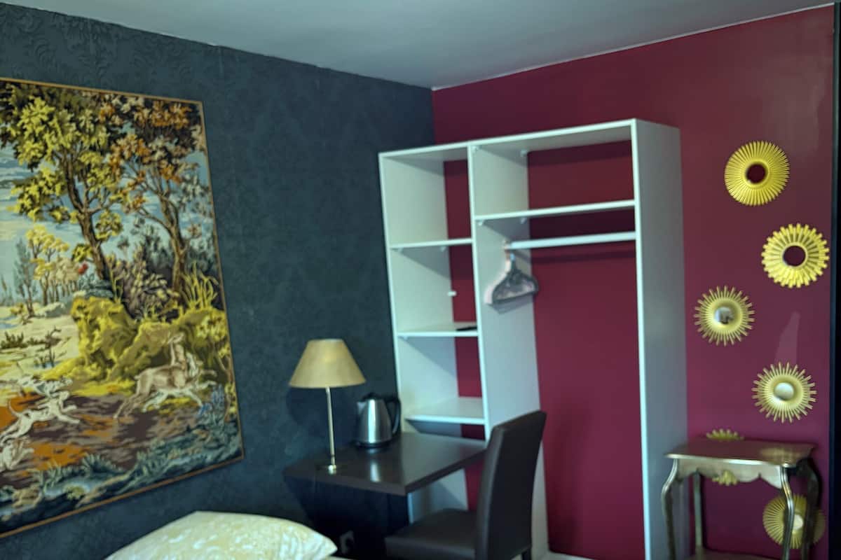 Ein Hotelzimmer mit Bett, Schreibtisch, Stuhl, Kleiderschrank und einem Bild an der Wand.