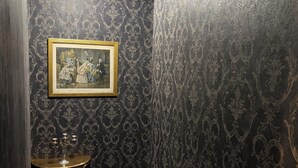Ein schmaler Korridor mit dunklem, gemustertem Wandteppich, einem gerahmten Bild an der Wand und einem kleinen Tisch mit einem Kandelaber.